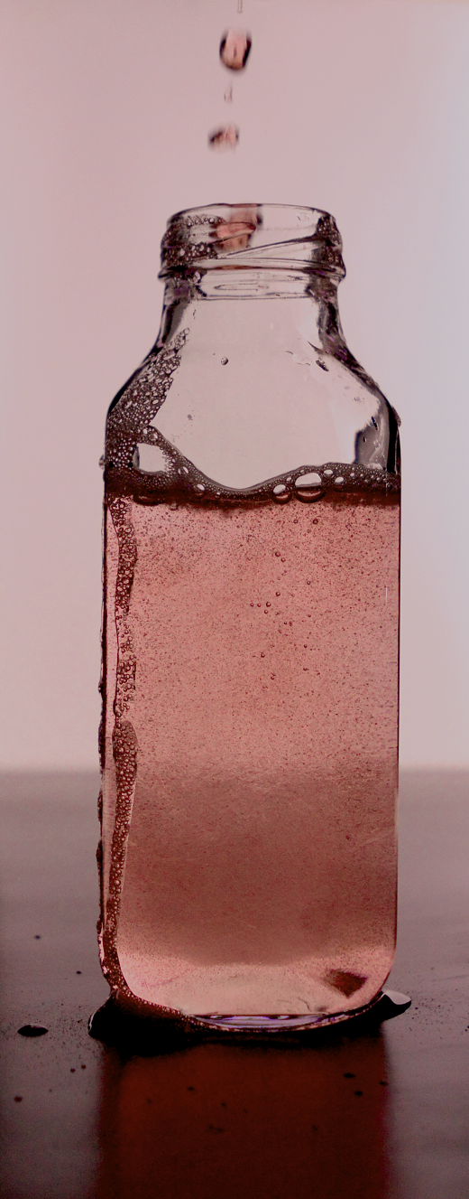 A red, transparent liquid being poured into a jar